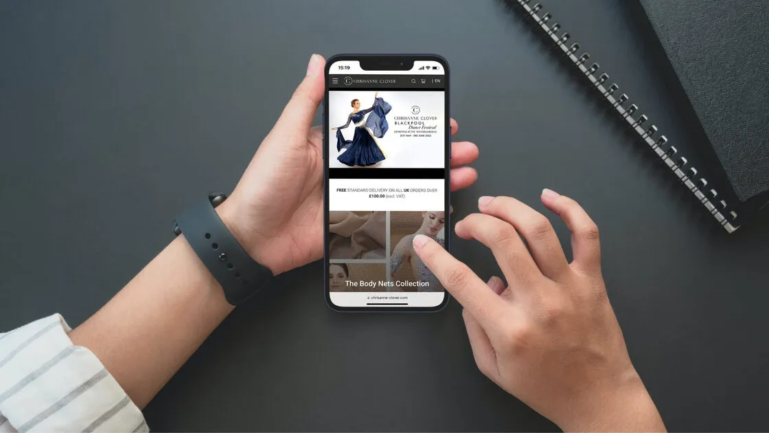 The Chrisanne Clover home page open on a phone held in both hands, with a collection banner and product tiles.
