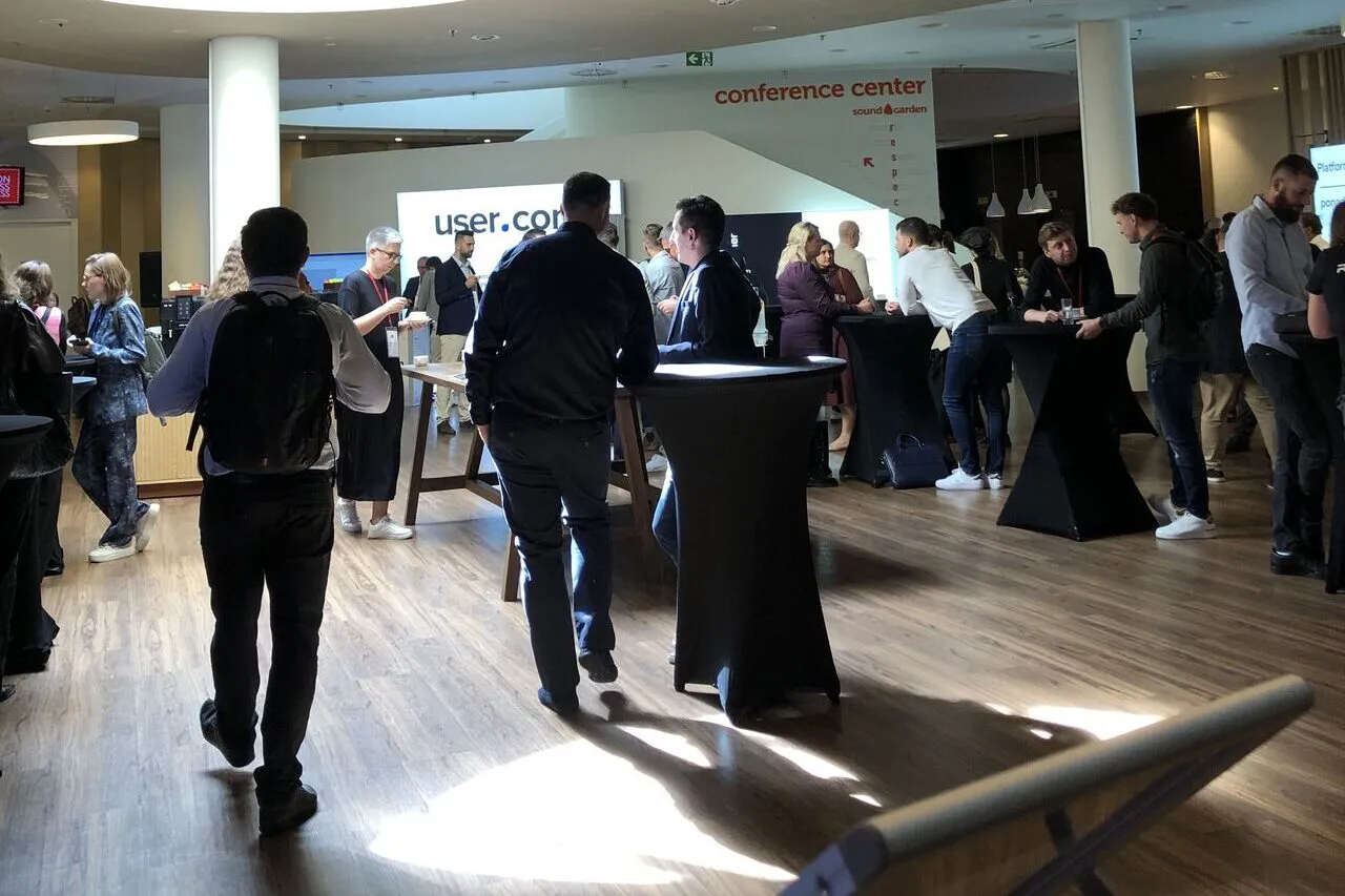 A conference foyer: attendees talking at cocktail tables under a conference center sign.