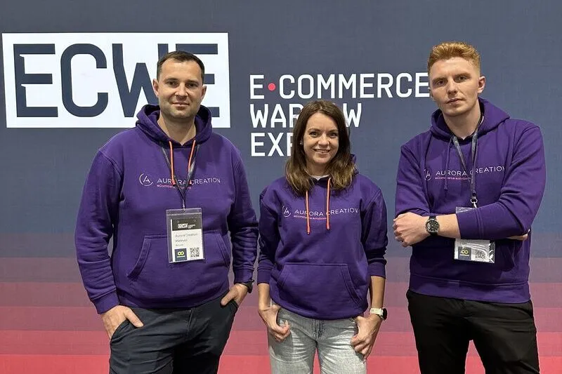 Three people from Aurora Creation in company hoodies in front of the E‑Commerce Warsaw Expo backdrop.