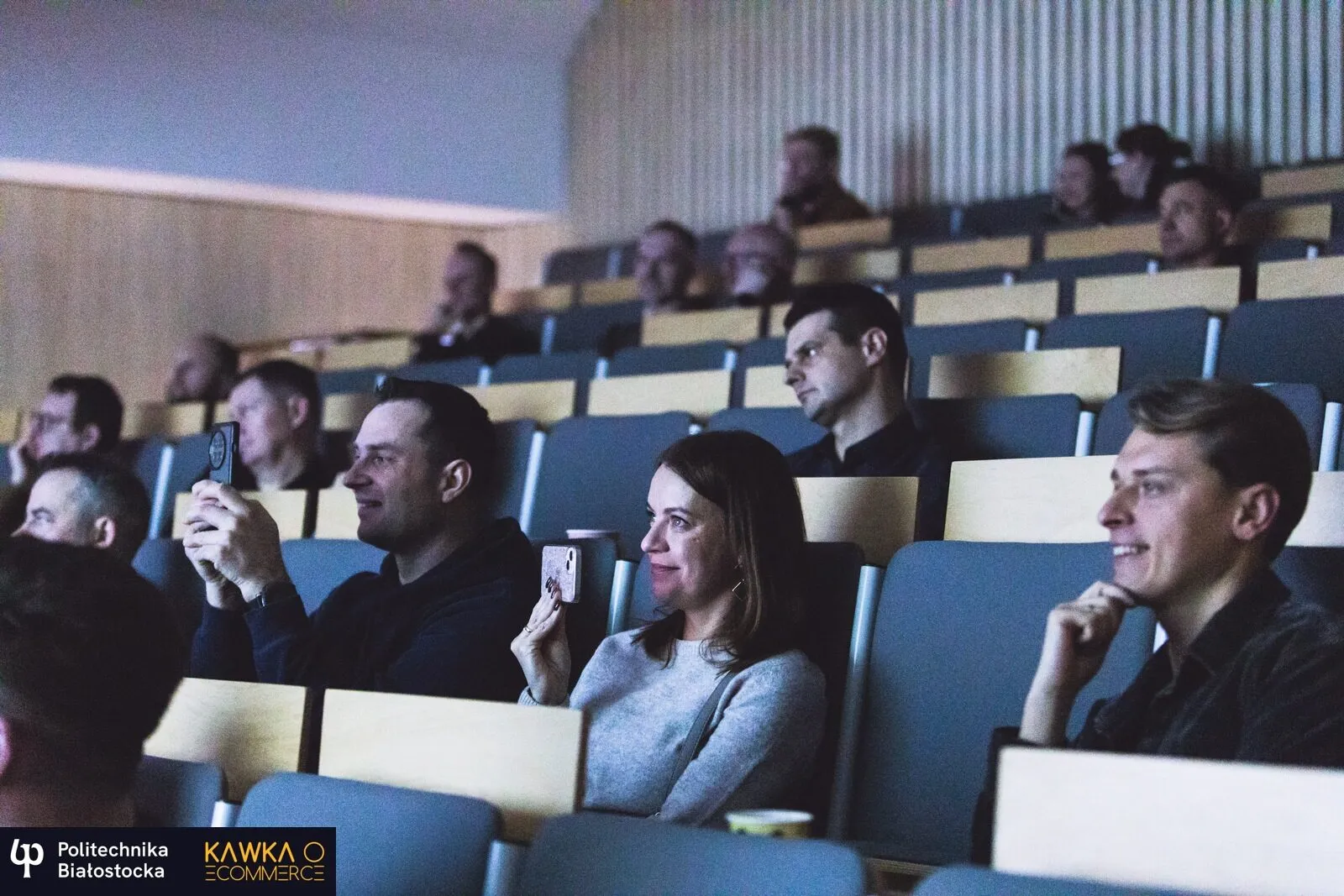 Attendees in a lecture hall during a talk, some of them filming it on their phones.